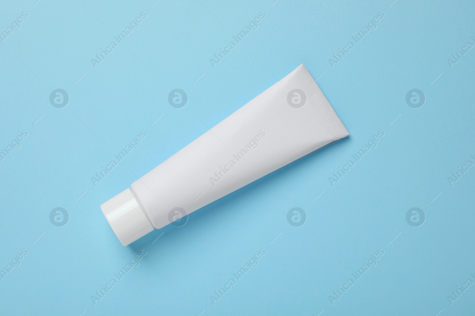 Photo of Blank tube of toothpaste on light blue background, top view