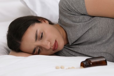 Photo of Depressed woman lying on bed near overturned bottle with antidepressants