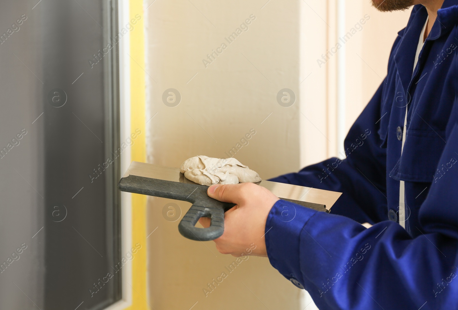 Photo of Professional worker with putty knifes and plaster near window indoors, closeup. Interior repair