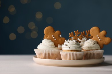 Photo of Tasty Christmas cupcakes on white wooden table against blurred festive lights