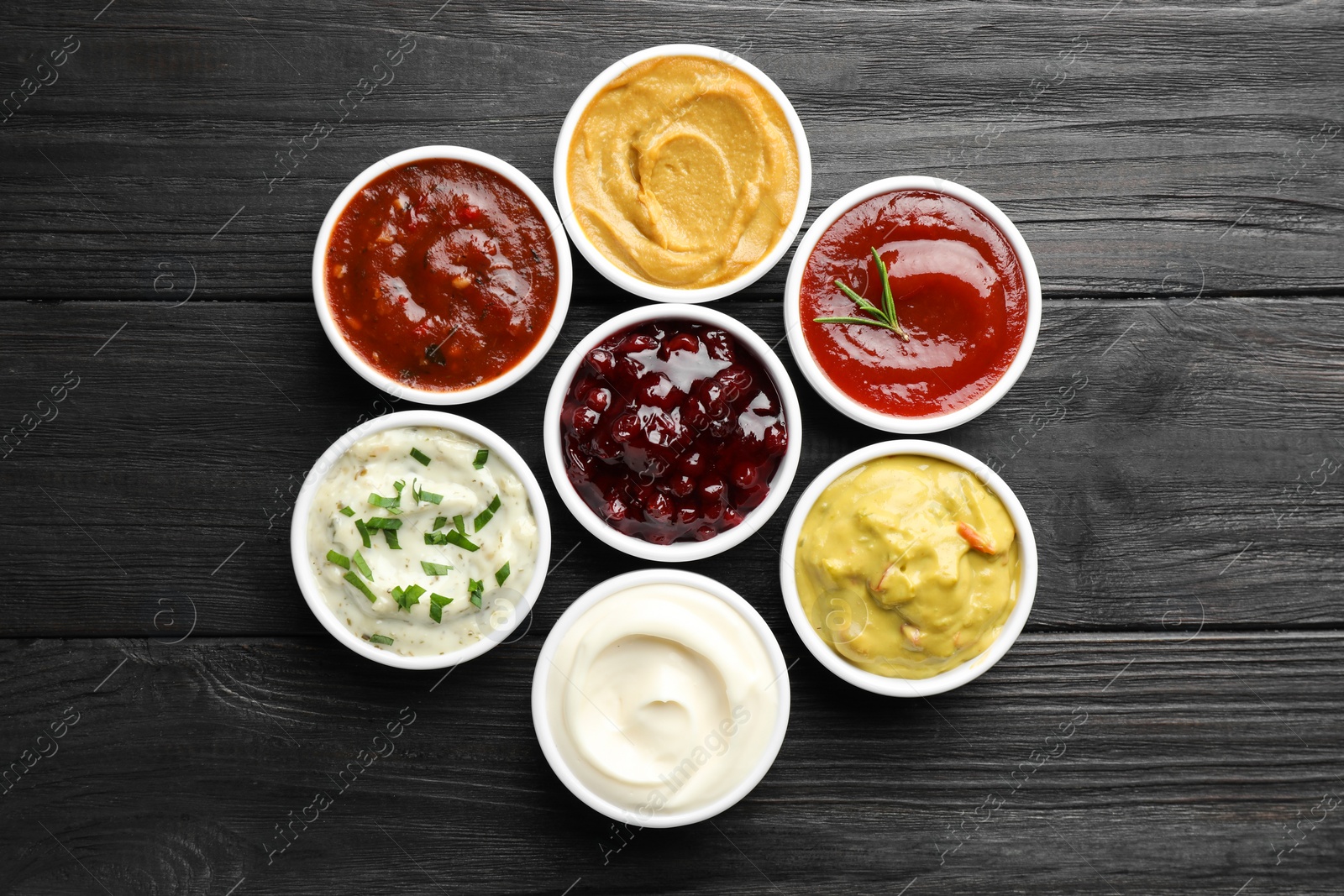 Photo of Different tasty sauces in bowls on black wooden table, flat lay