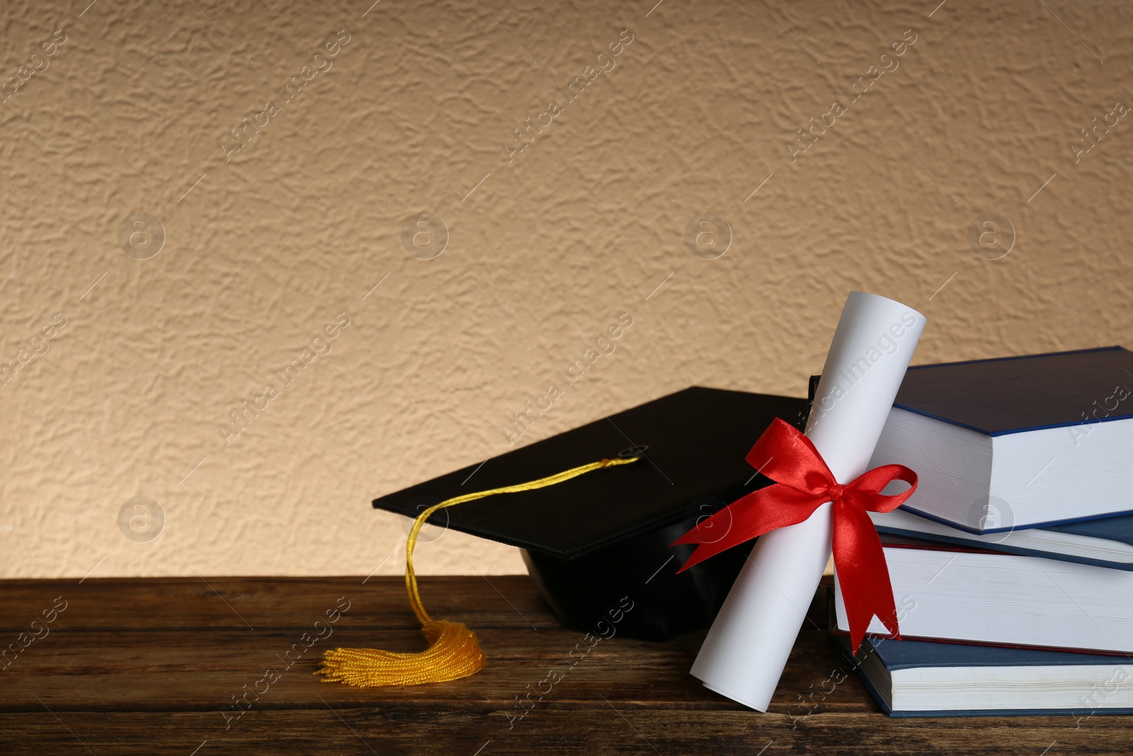 Photo of Graduation hat, books and diploma on wooden table. Space for text