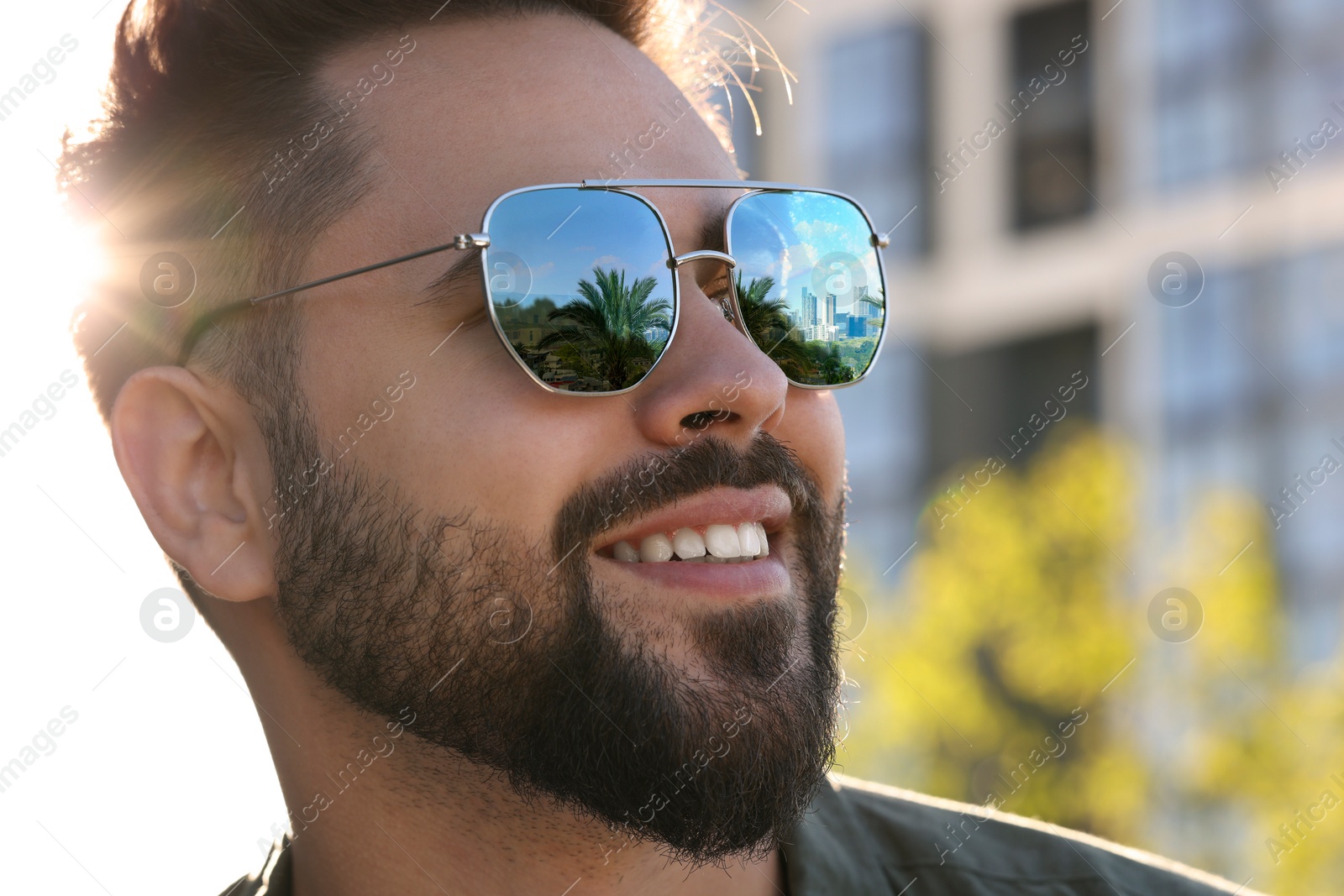 Image of Man in sunglasses on sunny day outdoors. Cityscape with palm trees reflecting in lenses