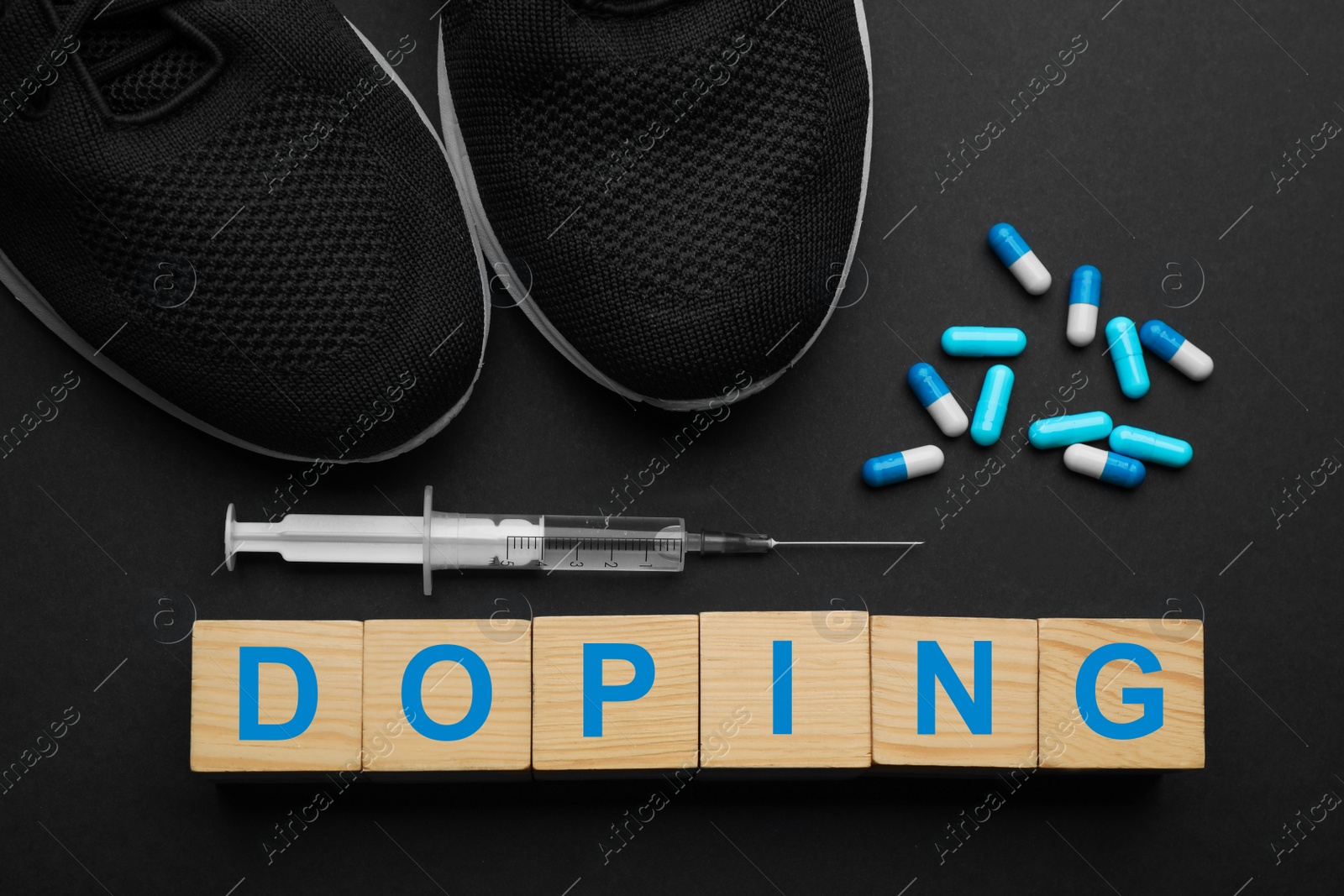 Photo of Wooden cubes with word Doping, sport shoes and drugs on black background, flat lay