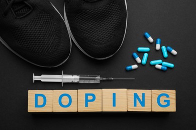 Photo of Wooden cubes with word Doping, sport shoes and drugs on black background, flat lay