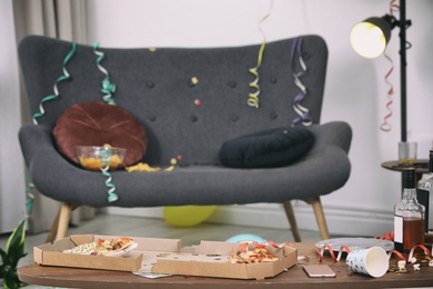 Photo of Table with pizza leftovers and alcohol in messy room interior. After party chaos