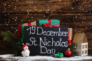 Slate board with text 19 December St. Nicholas Day, gift boxes and festive decor on wooden table