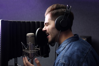 Photo of Young singer with microphone recording song in studio