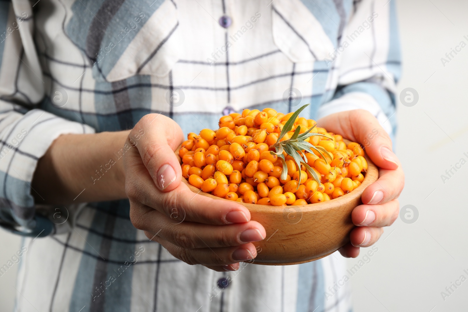 Photo of Woman holding bowl with fresh ripe sea buckthorn on light background, closeup