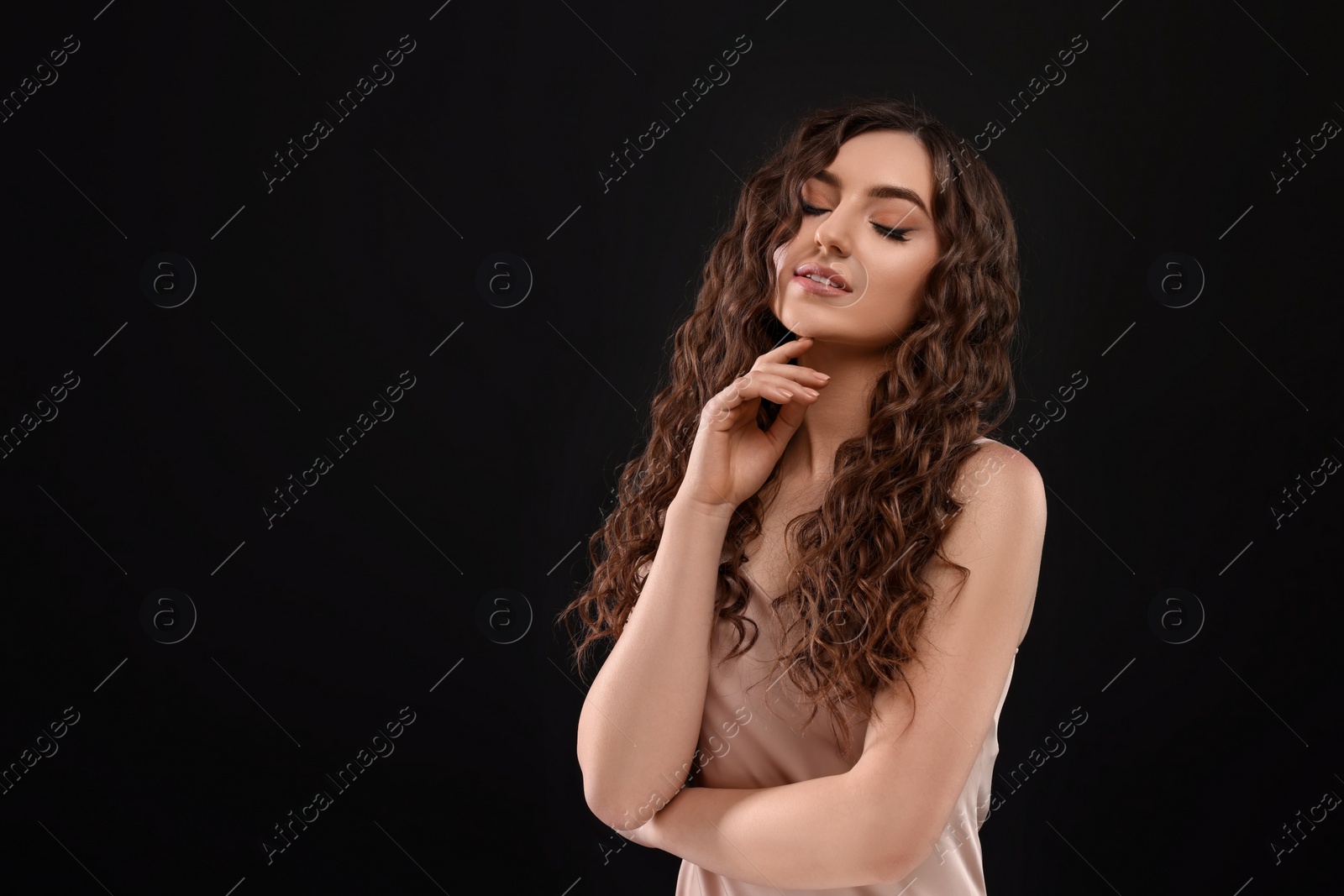 Photo of Beautiful young woman with long curly brown hair on black background, space for text