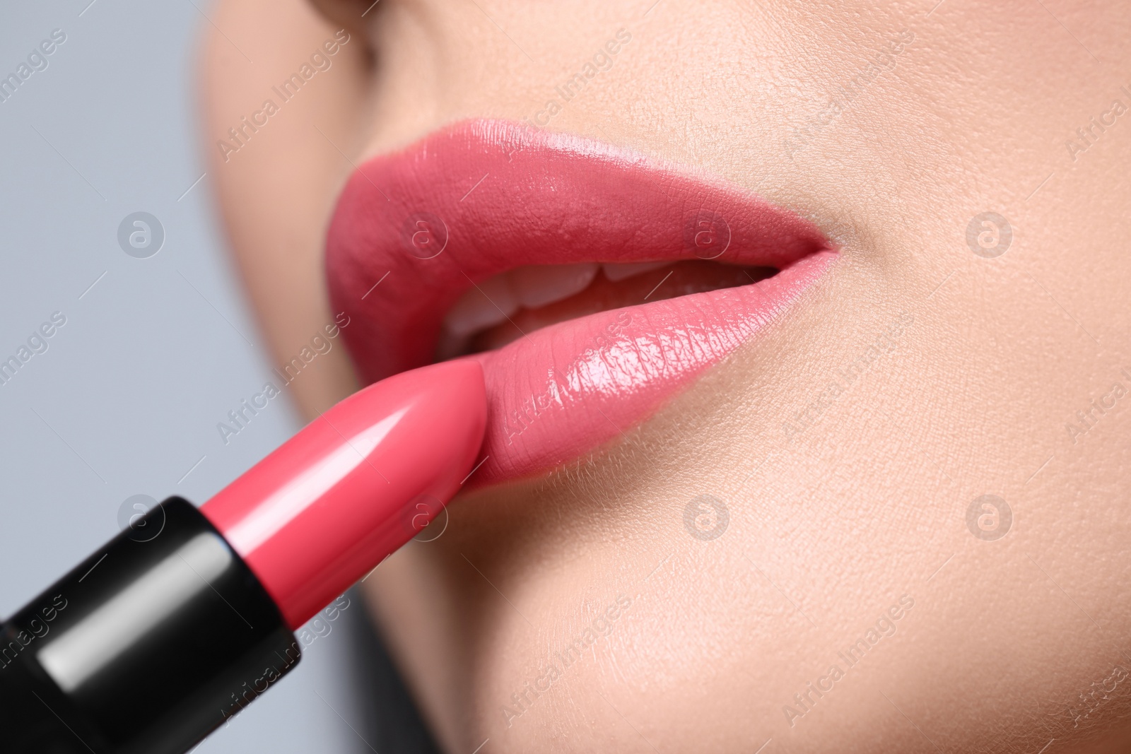 Photo of Young woman applying beautiful glossy lipstick on light background, closeup