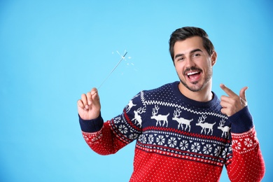 Portrait of young man in Christmas sweater with sparkler on light blue background