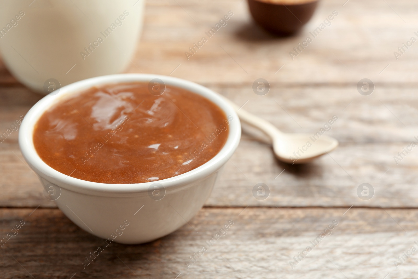 Photo of Bowl with caramel sauce on wooden table, closeup. Space for text