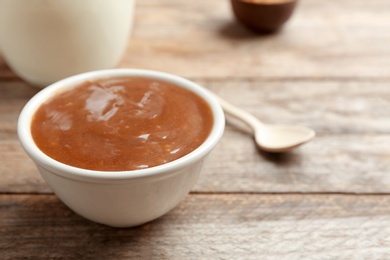 Photo of Bowl with caramel sauce on wooden table, closeup. Space for text