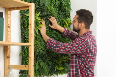 Photo of Man installing green artificial plant panel on white wall in room