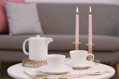 Cups of tea, teapot and burning candles on white coffee table indoors
