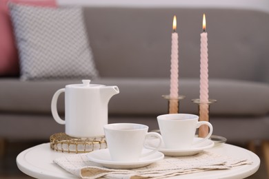 Photo of Cups of tea, teapot and burning candles on white coffee table indoors