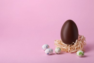 Photo of Decorative nest with tasty chocolate egg and candies on pink background. Space for text