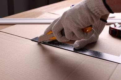 Worker cutting cardboard with utility knife and ruler, closeup