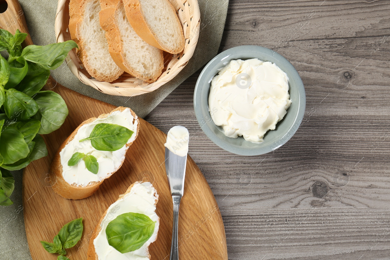 Photo of Delicious sandwiches with cream cheese and basil leaves on wooden table, flat lay