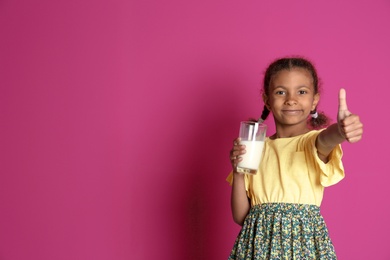 Adorable African-American girl with glass of milk on color background