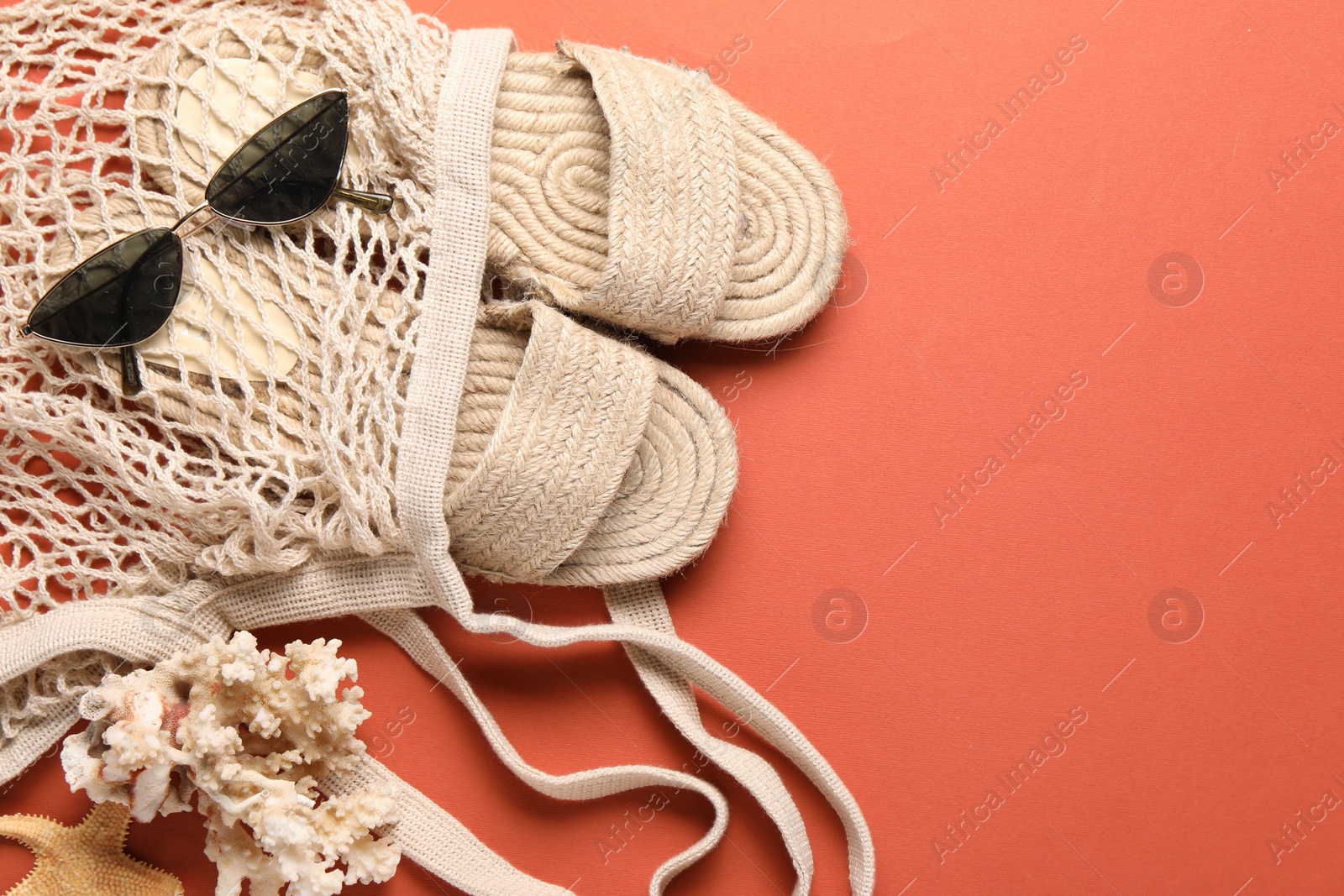 Photo of String bag, sunglasses, slippers, starfish and coral on color background, top view. Space for text