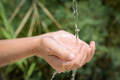 Photo of Pouring water into kid`s hands outdoors, closeup