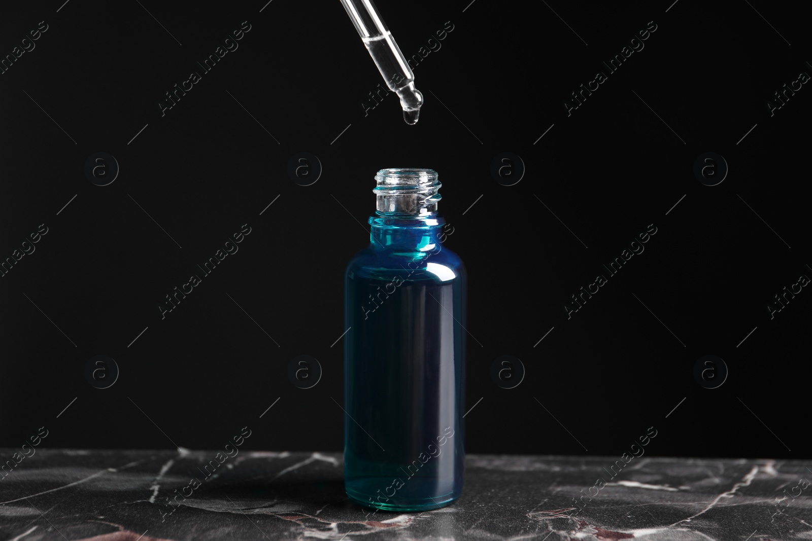 Photo of Dripping cosmetic serum from pipette into bottle on grey marble table