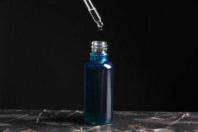 Photo of Dripping cosmetic serum from pipette into bottle on grey marble table