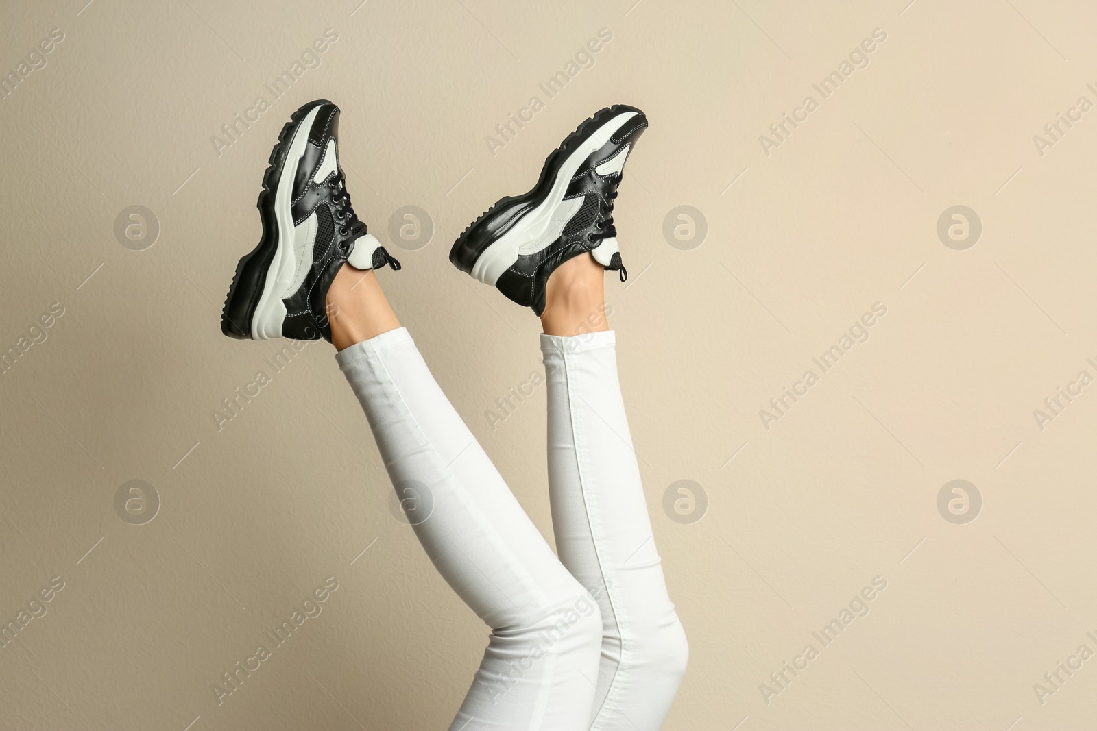 Photo of Woman wearing sneakers on beige background, closeup