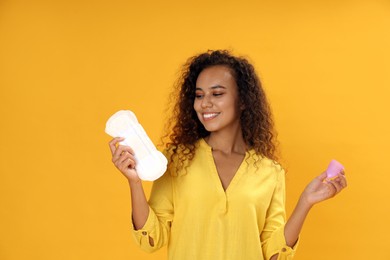 Photo of Young African American woman with menstrual cup and pad on yellow background