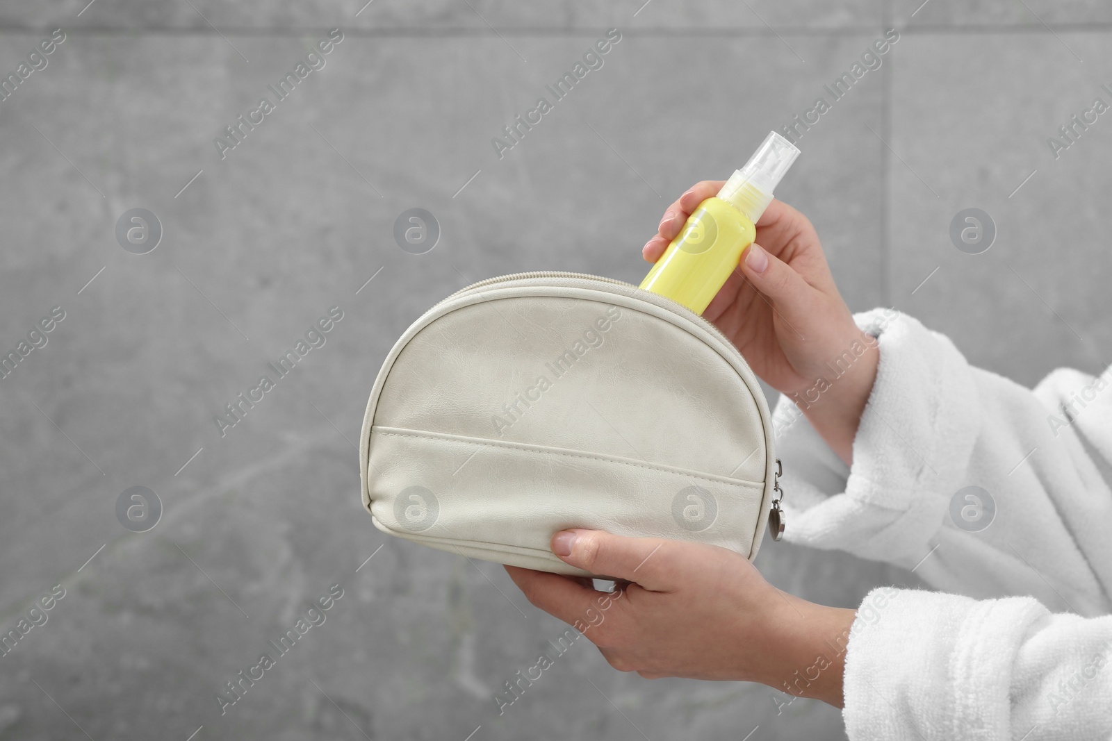 Photo of Woman packing cosmetic travel kit near grey wall closeup and space for text. Bath accessories