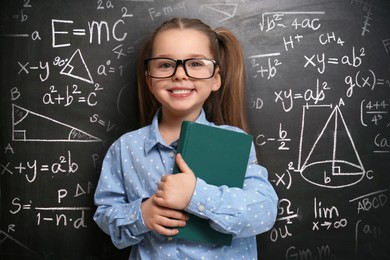 Cute little child wearing glasses near chalkboard with different formulas