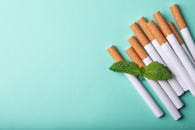 Photo of Menthol cigarettes and mint on turquoise background, flat lay. Space for text