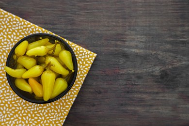 Photo of Bowl of pickled yellow jalapeno peppers on wooden table, top view. Space for text