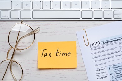 Photo of Reminder note with words Tax Time, documents, glasses and keyboard on white wooden table, flat lay