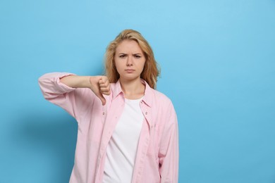 Photo of Dissatisfied young woman showing thumb down gesture on light blue background. Space for text