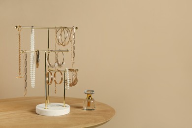Holder with set of luxurious jewelry and perfume on wooden table near beige wall, space for text