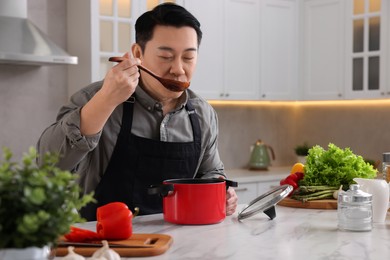 Photo of Cooking process. Man tasting dish at countertop in kitchen