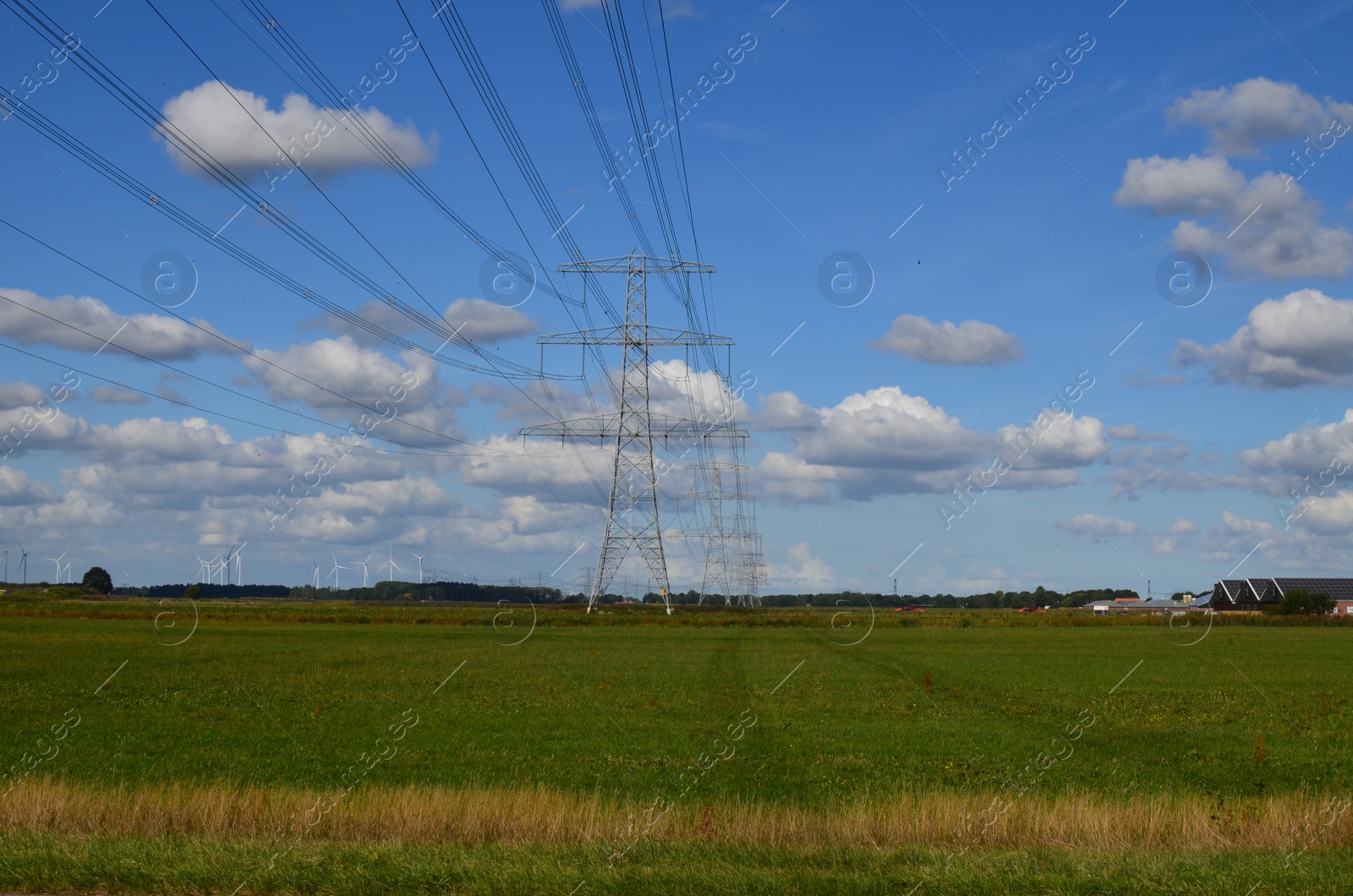 Photo of High voltage towers with electricity transmission power lines in field on sunny day