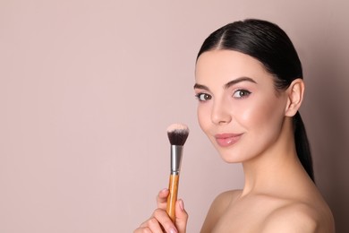 Photo of Beautiful young woman applying face powder with brush on dusty rose background. Space for text