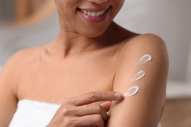 Photo of Beautiful young woman applying body cream onto arm on blurred background, closeup