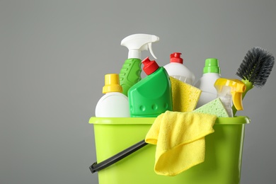 Photo of Bucket with cleaning products and tools on grey background, closeup