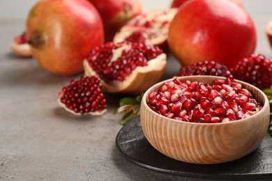 Photo of Delicious ripe pomegranate kernels in bowl on grey table. Space for text