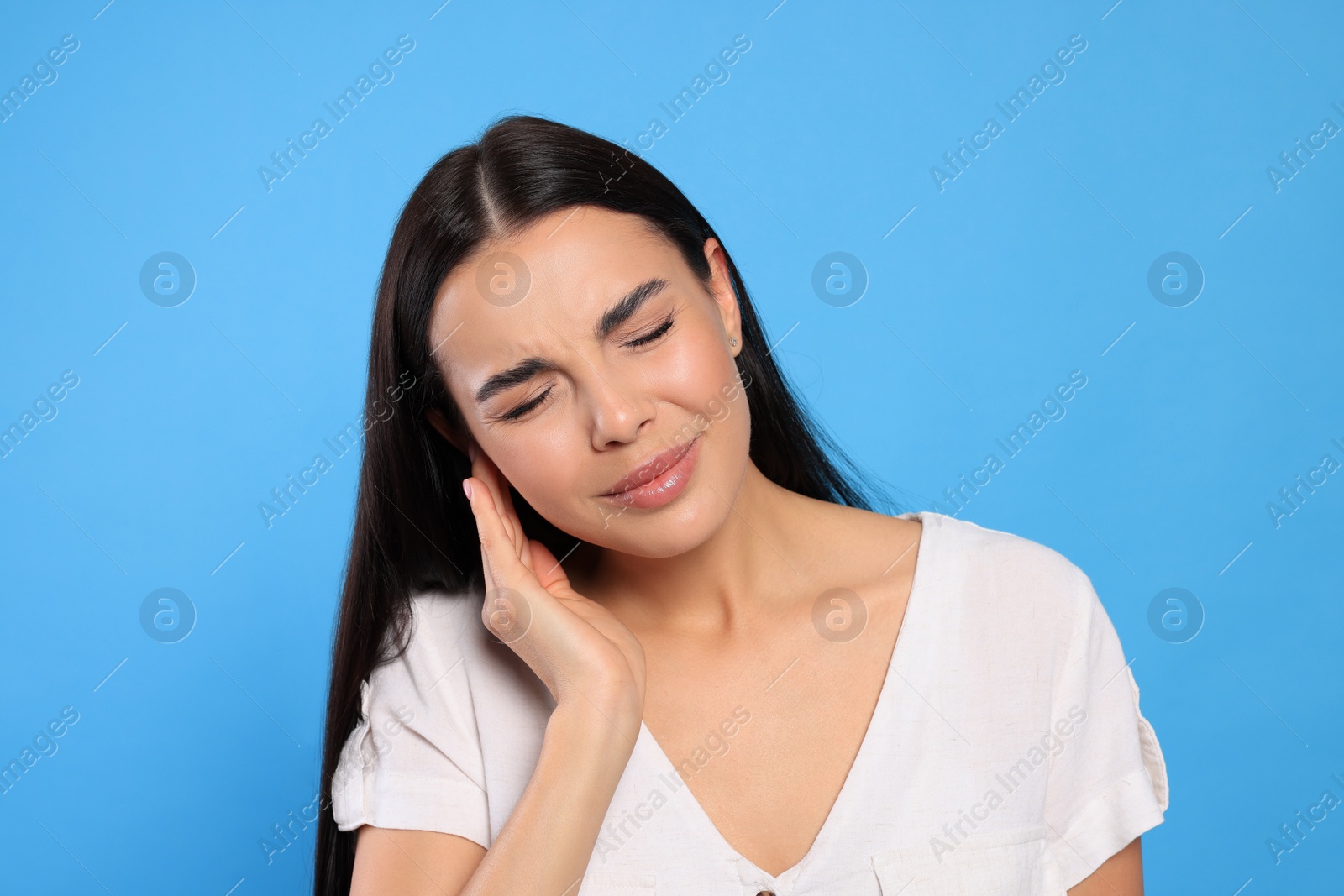 Photo of Young woman suffering from ear pain on light blue background