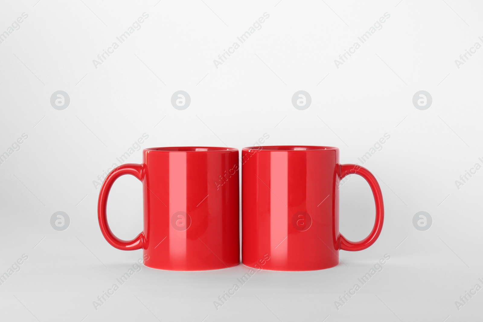 Blank red ceramic mugs on light background Photo of Blank red ceramic mugs on light background
