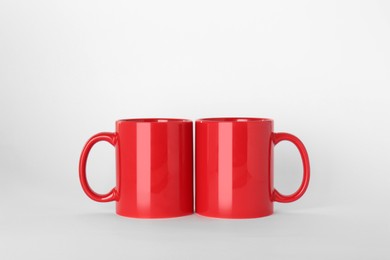 Photo of Blank red ceramic mugs on light background