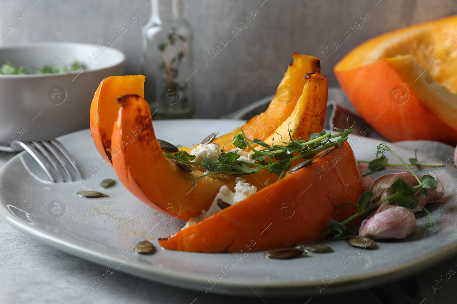 Photo of Baked pumpkin slices served with cheese, microgreens, seeds and garlic on light table, closeup
