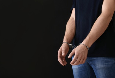 Man detained in handcuffs against dark background, space for text. Criminal law