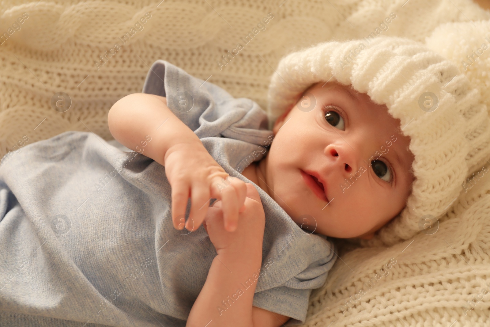 Photo of Cute little baby wearing white warm hat on knitted blanket